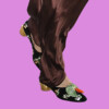 A close-up of a person's foot wearing a black velvet shoe with floral embroidery, paired with brown satin pants, bla bla.