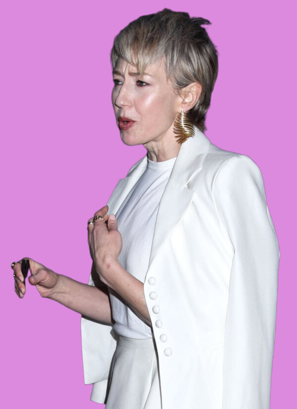 A woman with short blonde hair wearing a white suit and gold earrings, holding a black item, in an urban setting at night, bla bla.