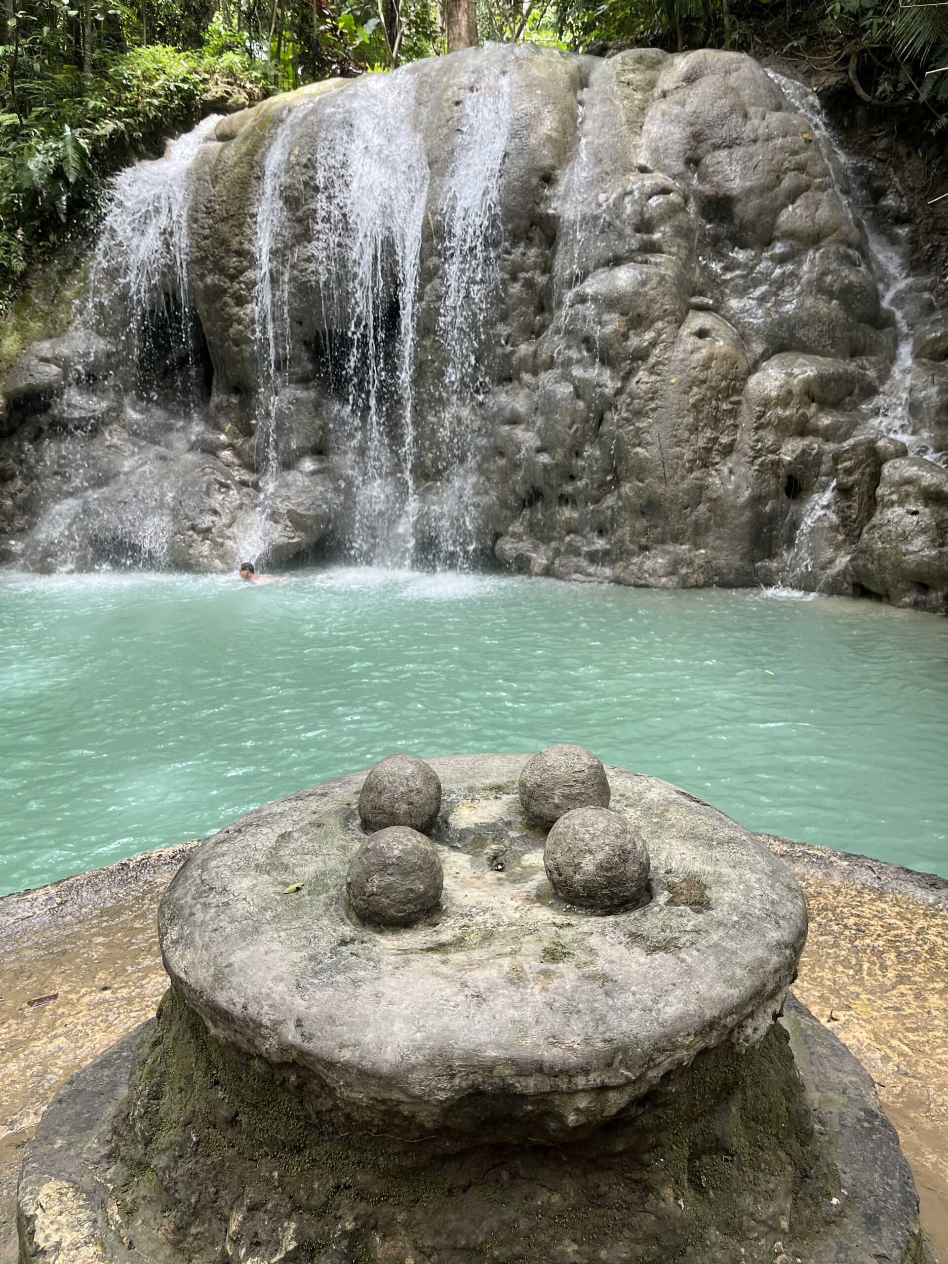 Stone table with four round stones near a waterfall. Tranquil pool of water.