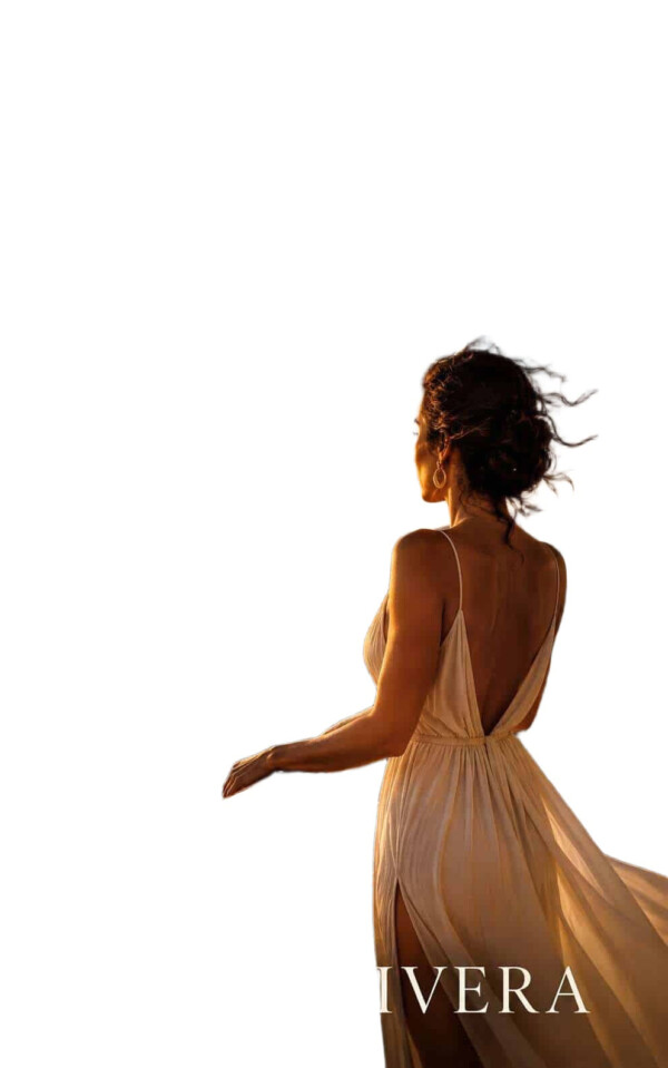 A woman with curly hair wearing a flowing beige dress, standing with her back to the camera, against a white background. bla bla.